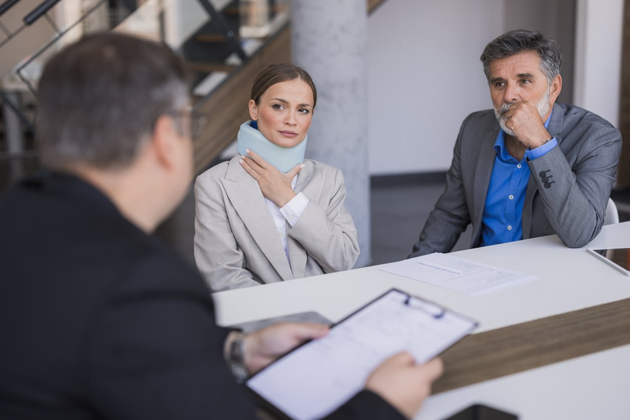 injured woman in neck brace and her personal injury lawyer at negotiations with another attorney