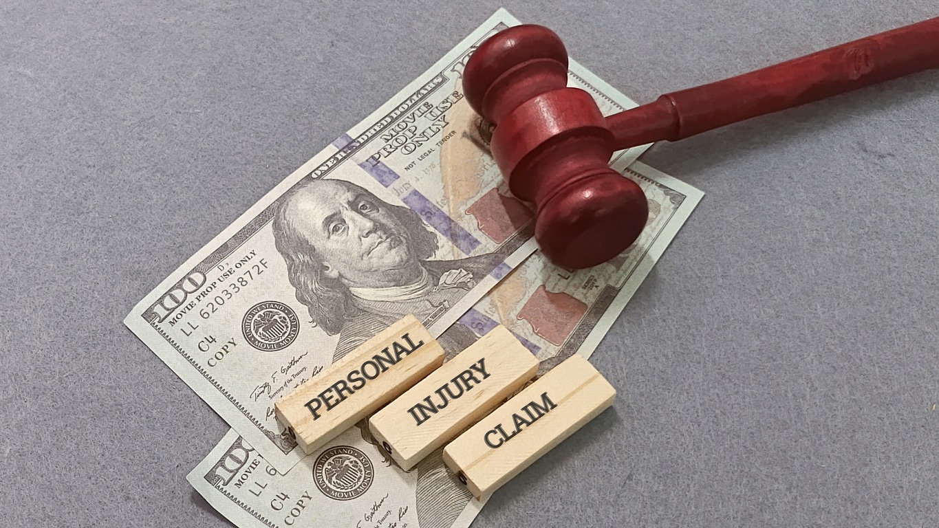 Personal injury claim settlement concept -wooden blocks spelling out the words resting on hundred dollar bills beneath a wooden judge's gavel.